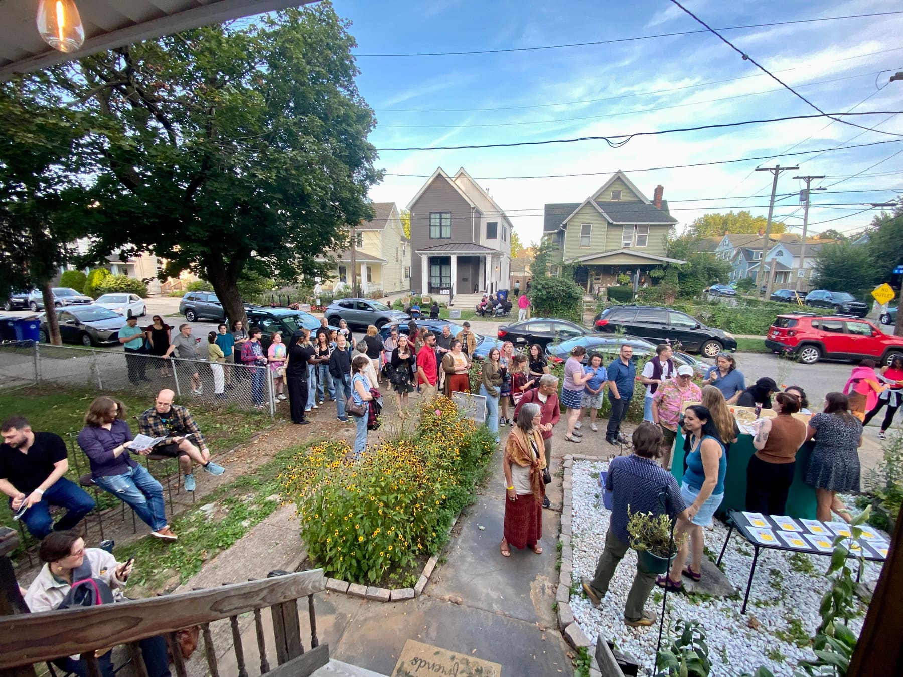 Seen from a porch at dusk, a crowd with programs fills a front yard and spills onto the street between shows